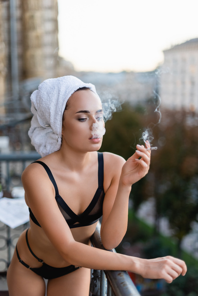 jovem sexy em roupa interior preta com toalha na cabeça fumar cigarro na varanda - Foto, Imagem