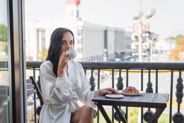 brunetka žena v bílém rouchu pití čaje a posezení na balkóně - Fotografie, Obrázek