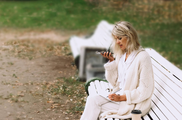 Młoda bizneswoman siedzi na ławce w parku i rozmawia przez telefon. - Zdjęcie, obraz