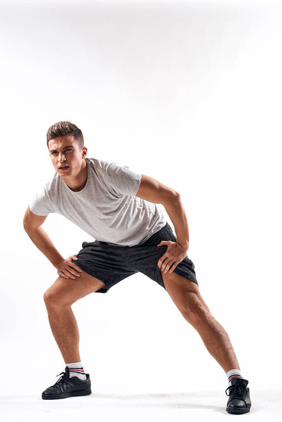 Ein Sportler in kurzen Hosen und einem durchgehenden T-Shirt macht auf hellem Hintergrund Übungen. - Foto, Bild