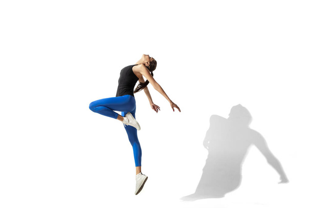 Beautiful young female athlete stretching on white studio background with shadows - Fotoğraf, Görsel