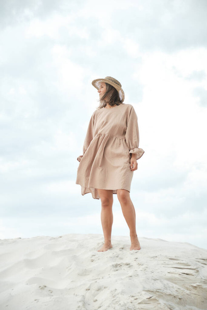 Stylish girl in trendy summer linen dress straw hat posing on the sand. Boho style. - Foto, immagini