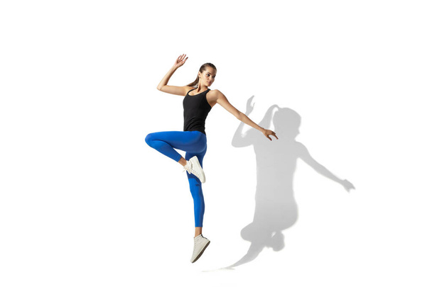 Beautiful young female athlete stretching on white studio background with shadows - 写真・画像