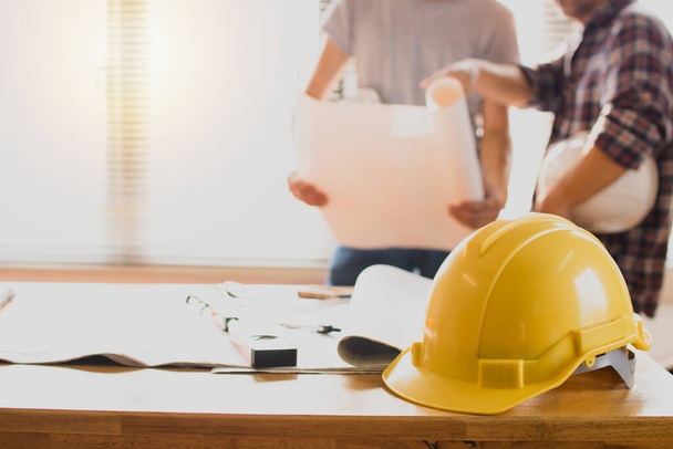 construction safety helmets on table with engineer holding blueprint background  - Fotó, kép
