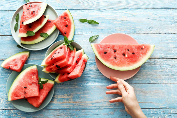 Fresh red watermelon slice, female hand on an blue rustic wood background with copy space. Top view. Summertime concept - Foto, Imagen