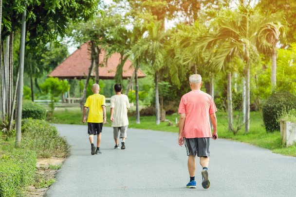 Vista posterior retrato de un anciano asiático en ropa de fitness caminar y trotar para una buena salud en el parque público. Corredor sénior en naturaleza. Hombre mayor disfrutando de la naturaleza pacífica. Concepto sanitario. - Foto, Imagen