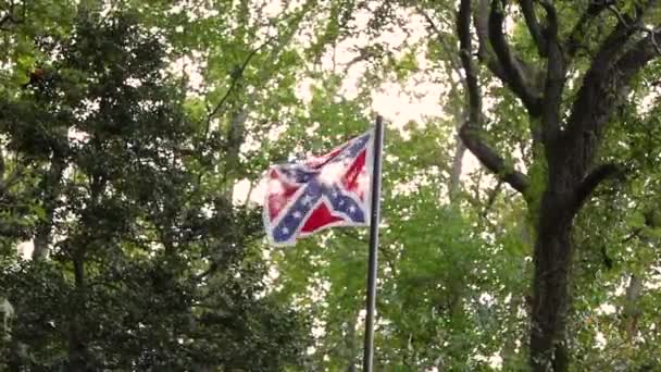 Подсвеченный флаг Конфедерации, развевающийся на ветру на флагштоке среди деревьев. Этот флаг расположен на кладбище Конфедерации недалеко от мыса Пойнтлук тюрьмы военного лагеря, используемого во время гражданской войны в США.. - Кадры, видео
