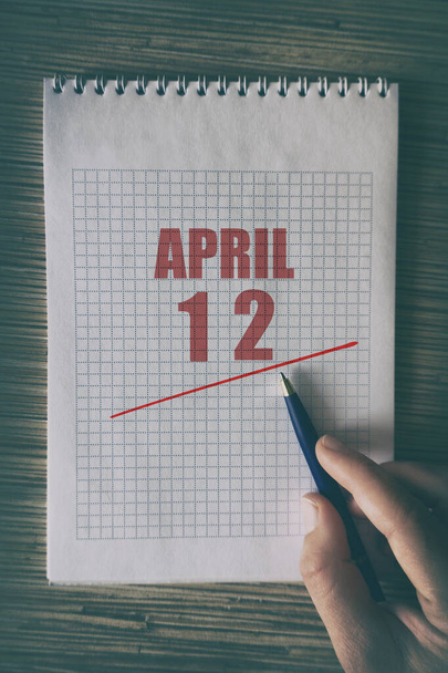 12 Απριλίου. Ημέρα 12 του μήνα, Κοντινό πλάνο του ανθρώπινου χεριού με στυλό στο σημειωματάριο με κόκκινο υπογράμμισε ημερομηνία. άνοιξη μήνα, ημέρα του έτους έννοια. - Φωτογραφία, εικόνα