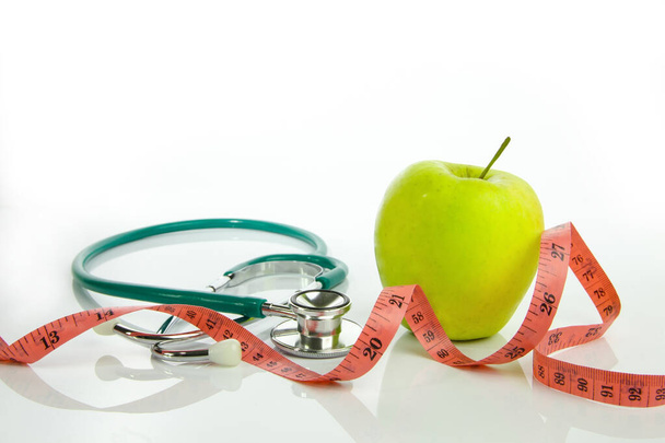 Zielone jabłko z miarą taśmy i stetoskopem na białym tle. Koncepcja diety i odchudzania - Zdjęcie, obraz