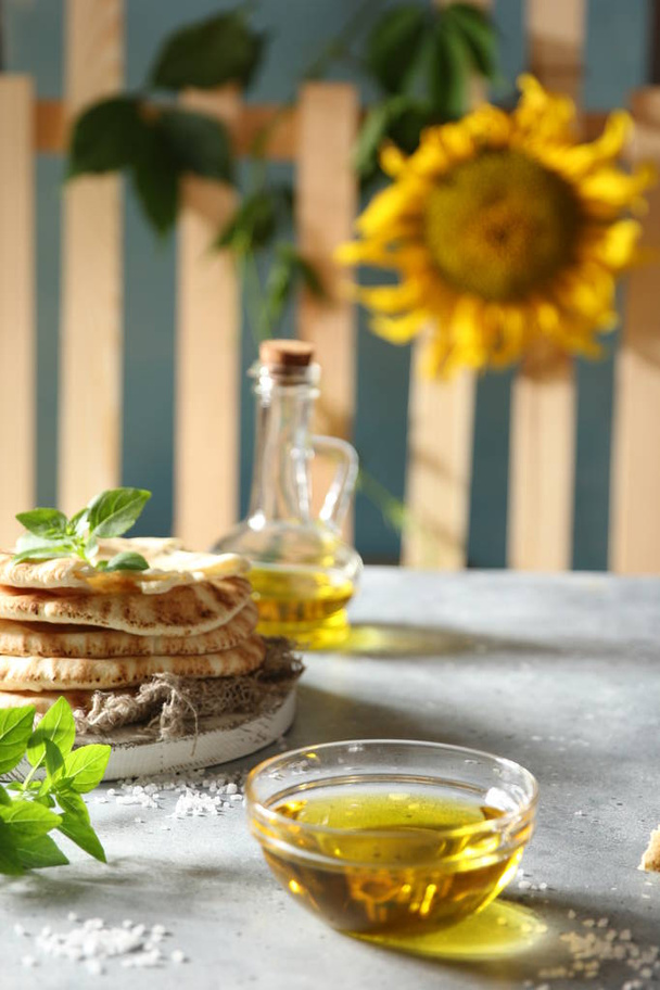Olive oil in a large transparent bowl, basil, salt and tortillas  on a light table. The village history. The fence and the sunflower. Background image, copy space - Foto, afbeelding