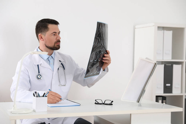 Orthopedist examining X-ray picture at desk in clinic - Zdjęcie, obraz