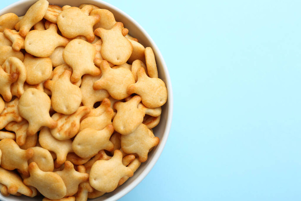 Delicious goldfish crackers in bowl on light blue background, top view. Space for text - Фото, зображення