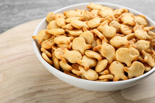 Delicious goldfish crackers in bowl on wooden board, closeup - Foto, afbeelding