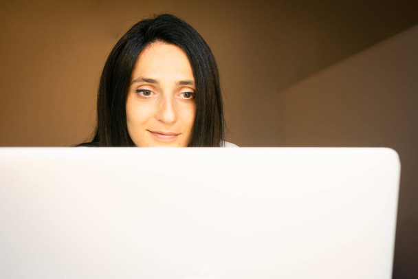 Молода біла жінка сидить у квартирі за білим робочим столом і дивиться прямо вперед. Концепція роботи з дому
. - Фото, зображення