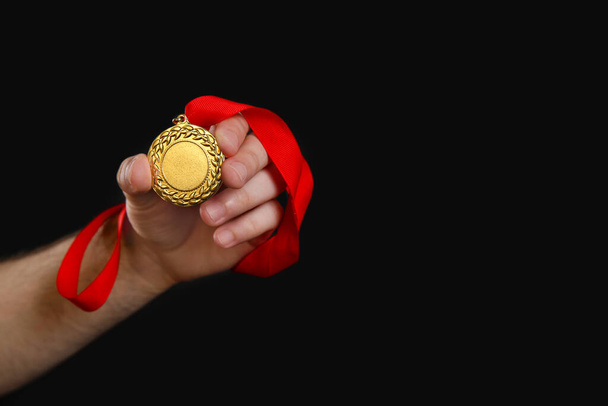 Man holding golden medal on black background, closeup. Space for design - Φωτογραφία, εικόνα