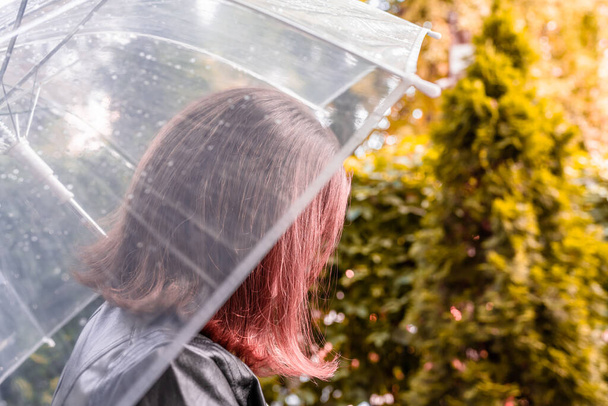 Autumn. Lonely sad woman under a transparent umbrella with rain drops walking in a park, garden. Rainy day landscape. Vintage Toned - Фото, изображение