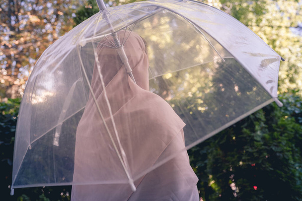Autumn. Lonely muslim woman in a headscarf under a transparent umbrella with rain drops walking in a park, garden. Rainy day landscape. Vintage Toned - Φωτογραφία, εικόνα