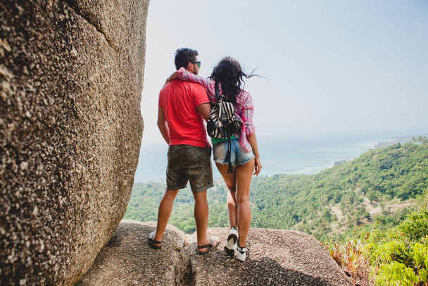 young happy hipster couple in love traveling around world, sightseeing, tropical romantic vacation in thailand, sitting on a rock, pointing finger, active tourism, summer - Photo, Image