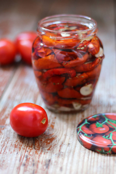 Kotitekoisia aurinkokuivattuja tomaatteja, joissa on yrttejä ja valkosipulia lasipurkissa, jossa on oliiviöljyä puupohjalla. Koruton tyyli, kopioi tilaa, lähikuva, ylhäältä näkymä. Tulosta keittiöön - Valokuva, kuva