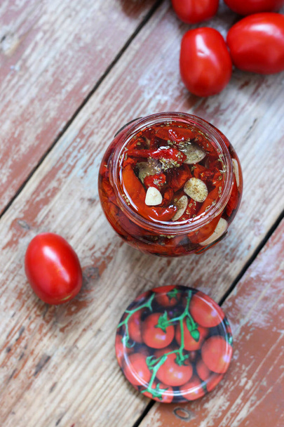 Kotitekoisia aurinkokuivattuja tomaatteja, joissa on yrttejä ja valkosipulia lasipurkissa, jossa on oliiviöljyä puupohjalla. Koruton tyyli, kopioi tilaa, lähikuva, ylhäältä näkymä. Tulosta keittiöön - Valokuva, kuva
