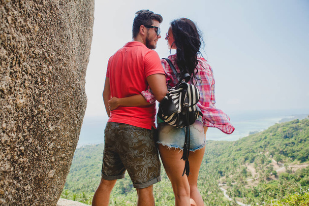 young happy hipster couple in love traveling around world, sightseeing, tropical romantic vacation in thailand, sitting on a rock, pointing finger, active tourism, summer - Foto, afbeelding