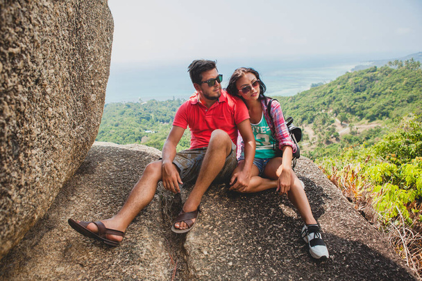 young happy hipster couple in love traveling around world, sightseeing, tropical romantic vacation in thailand, sitting on a rock, pointing finger, active tourism, summer - Foto, Imagen