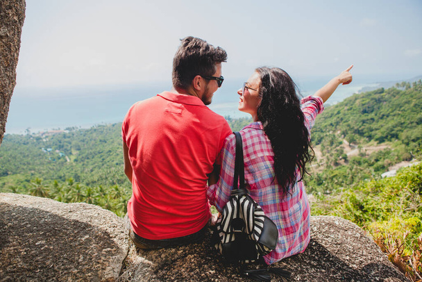 young happy hipster couple in love traveling around world, sightseeing, tropical romantic vacation in thailand, sitting on a rock, pointing finger, active tourism, summer - Foto, immagini