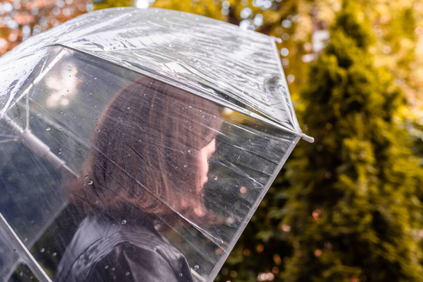 Autumn. Lonely redhead girl under a transparent umbrella with rain drops walking in a park, garden. Rainy day landscape - Zdjęcie, obraz