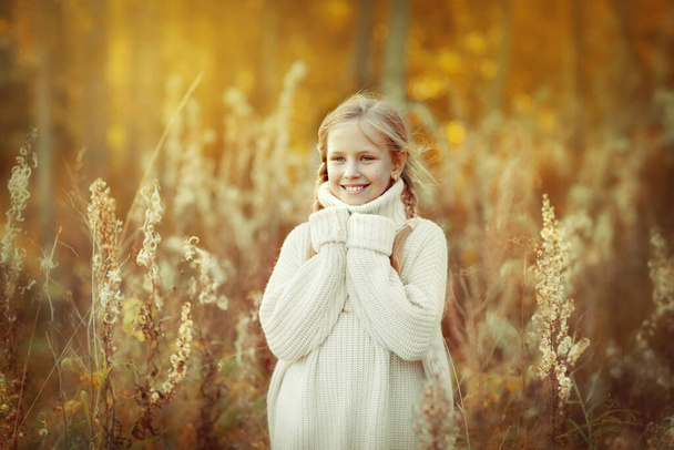 Retrato de una hermosa niña en un suéter blanco y cálido sonriendo en el bosque de otoño. - Foto, imagen