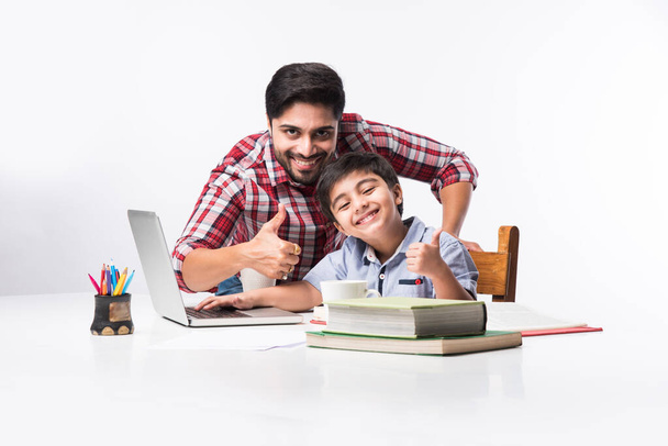 Aranyos indiai fiú apa vagy férfi tutor csinál házi feladatot otthon segítségével laptop és könyvek - online iskoláztatási koncepció - Fotó, kép