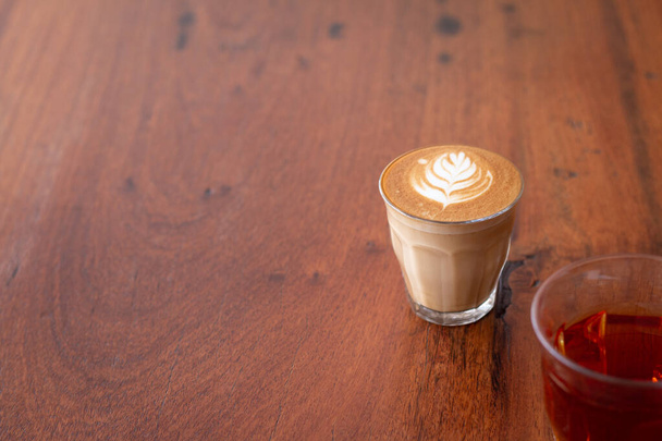 Piccolo Latte arte en vaso pequeño con té caliente en escritorio de madera. - Foto, Imagen