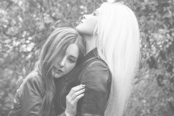 Two attractive women in autumn park wear leather jackets. Beautiful stylish city ladies on a walk. Concept of woman's friendship and sister relationship - Photo, Image