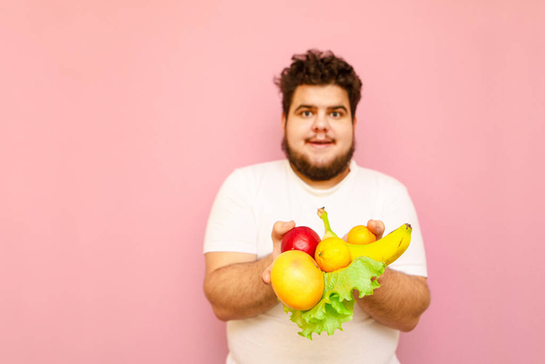 Cara gordo positivo em t-shirt branca isolado em fundo rosa com comida saudável, contém frutas e verduras. Brinde engraçado isolado em fundo rosa com frutas, conceito de dieta. Espaço de cópia - Foto, Imagem