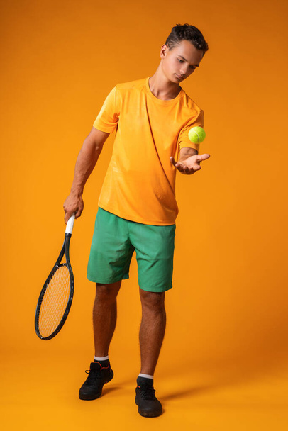 Full-length portrait of a tennis player man in action against orange background - Фото, изображение