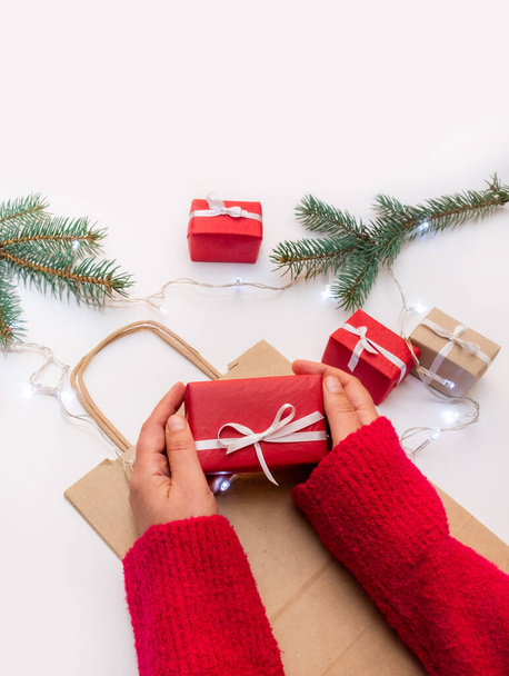 Kädet pitävät lahjapakkausta juhlallisella taustalla pussilla, laatikoilla ja joulukuusella - Valokuva, kuva