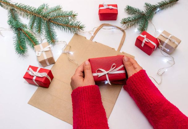 Hands hold gift's box on a festive background with bag, boxes and christmas tree - 写真・画像