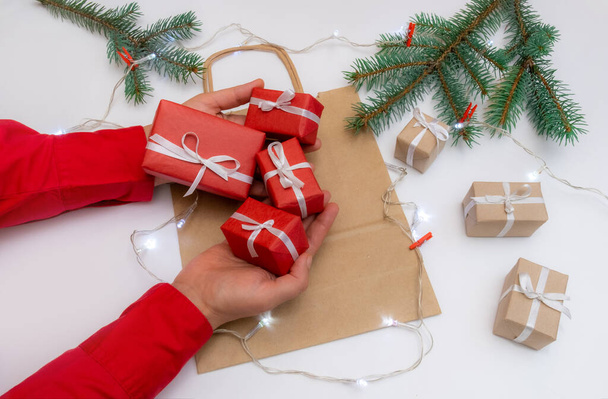 Χέρια κρατήστε κουτί δώρου σε ένα εορταστικό φόντο με τσάντα, κουτιά και χριστουγεννιάτικο δέντρο - Φωτογραφία, εικόνα