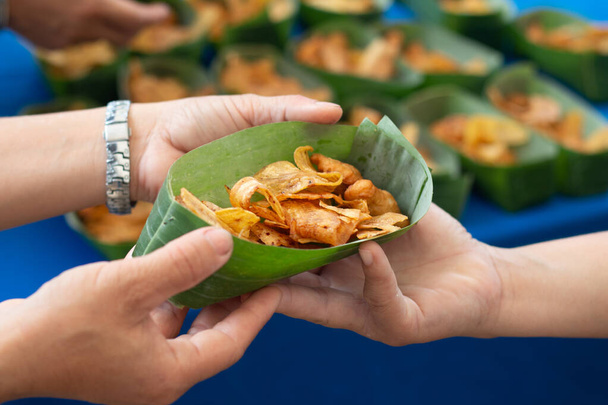 Manos sosteniendo chips de plátano en la copa de hojas de la naturaleza. - Foto, imagen
