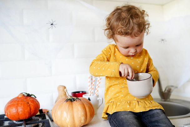 Linda niña están sentados en la mesa cerca de las calabazas de Halloween en casa y comer postre sabroso - Foto, Imagen