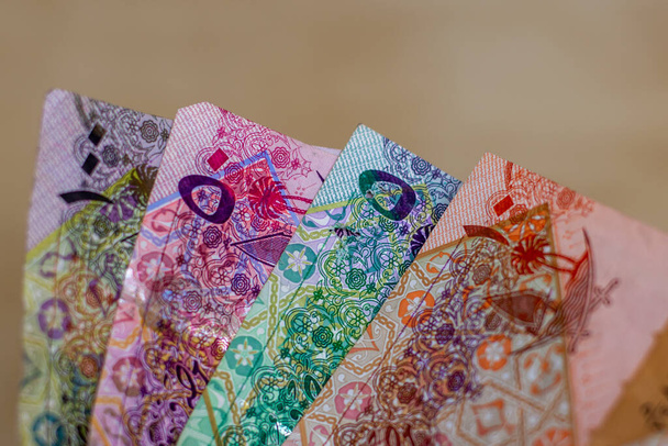 Moneda de Qatar - cientos de billetes riales o riales se extienden sobre un fondo marrón. Cambio de moneda. - Foto, Imagen