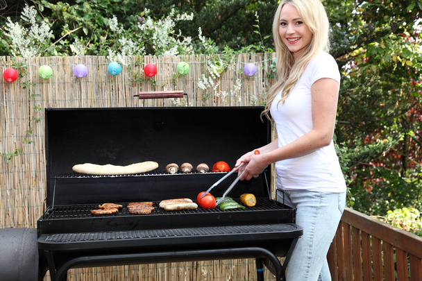 Beautiful blond woman barbecuing on a patio - Photo, image