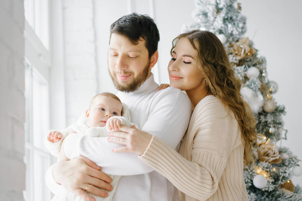 Une belle famille heureuse avec un petit enfant sont sur le fond des intérieurs de Noël - Photo, image