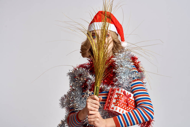mujer emocional con ramas de un árbol festivo y una gorra de oropel roja en su sudor de rayas en la cabeza - Foto, imagen