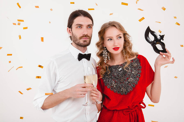 young stylish couple in love celebrating new year, happy disco party, wearing red dress, mask, bow tie, holding glasses of champagne, luxury and hipster style, fashion jewelry - Photo, image