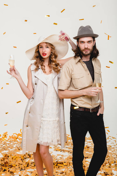 young stylish hipster couple in love, holding glasses and drinking champagne, toasting, celebrating disco party, having fun, golden confetti, trendy apparel, luxury cruise style, white background - Φωτογραφία, εικόνα