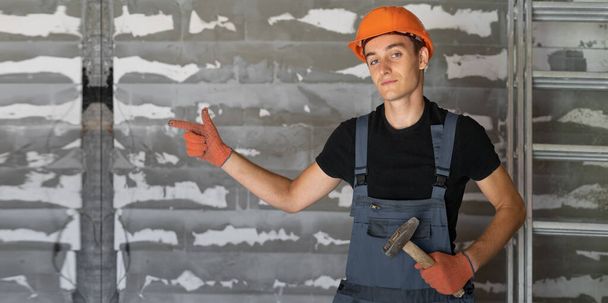 dělník s oranžovou helmou u kamenné zdi. ukazuje prstem na prázdné místo pro text. - Fotografie, Obrázek