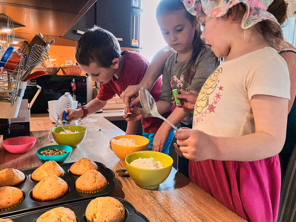 カップケーキを焼く子供たちのグループ,材料を準備,トッピング,クッキーを飾るためのスプリンクル.子供たちは料理を学び、自宅のキッチンで一緒に働いています。幸せな家庭の概念 - 写真・画像