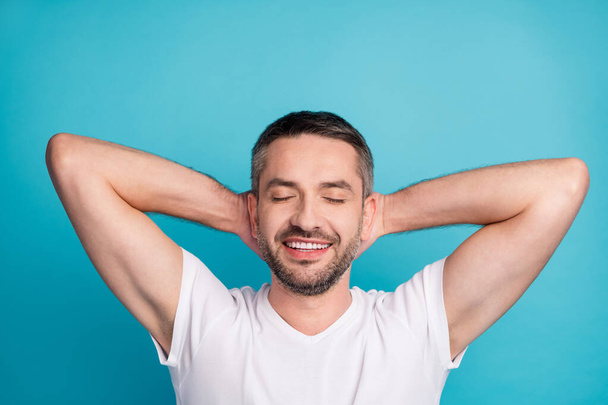 Close-up portrait of his he nice attractive dreamy cheerful cheery bearded guy wearing tshirt holding hands behind head having rest time isolated over bright vivid shine vibrant blue color background - Foto, Imagem