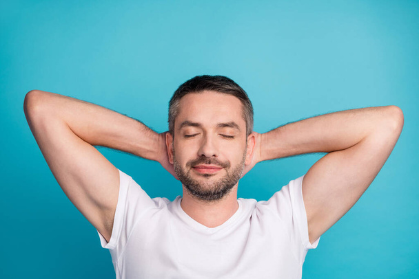Close-up portrait of his he nice attractive dreamy bearded guy wearing tshirt holding hands behind head resting isolated over bright vivid shine vibrant blue color background - 写真・画像