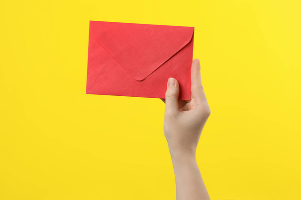 Woman holding red paper envelope on yellow background, closeup - Foto, Bild